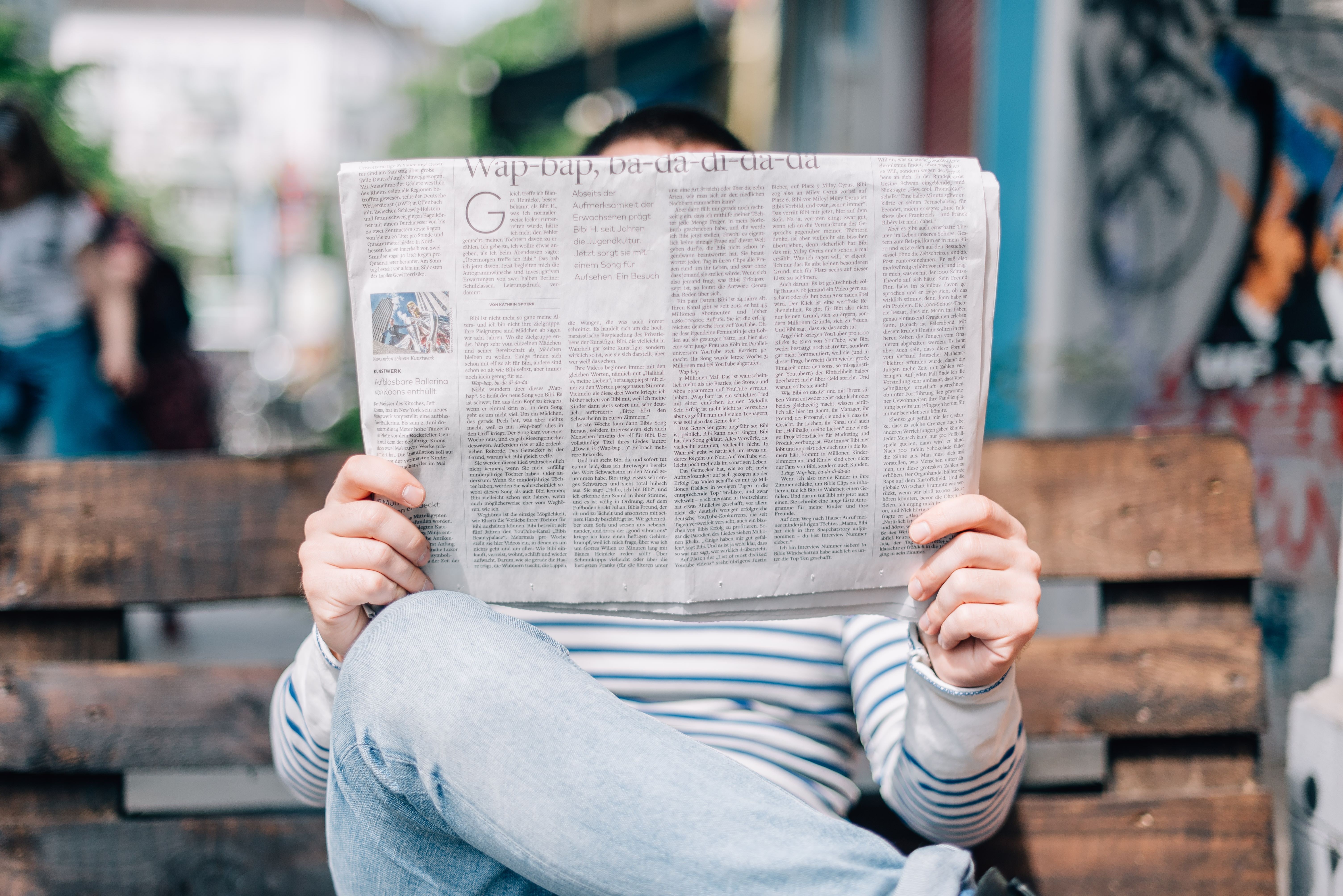 Man sitting on a bench holding up a newspaper